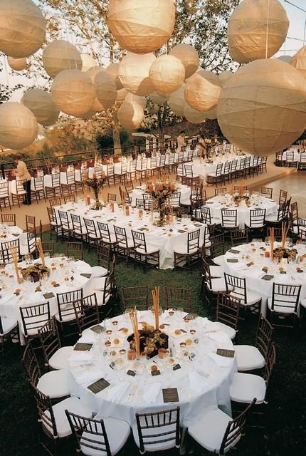 Réception en soirée dans un jardin : tables rondes dressées sous des lanternes en papier